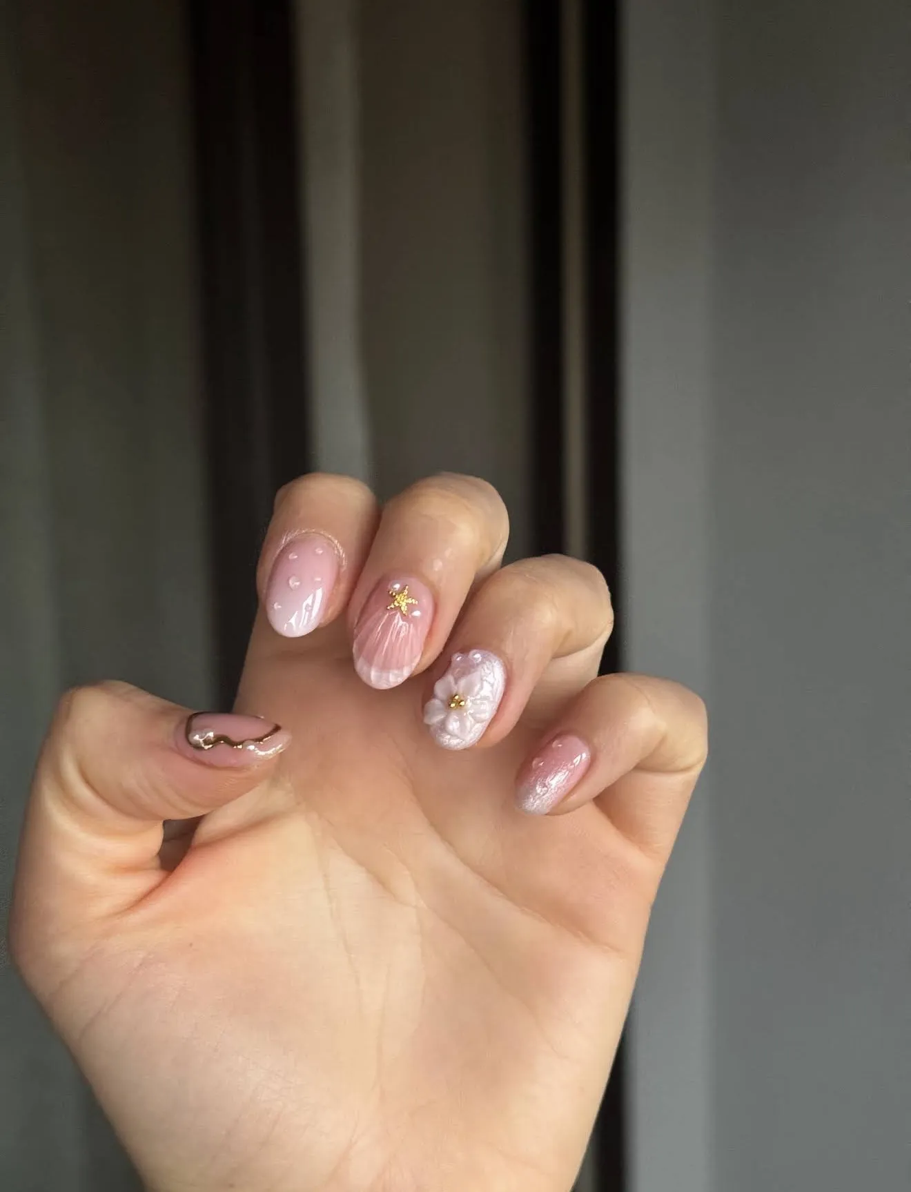 Short pink nails with seashell texture, a pearl flower and a gold starfish charm