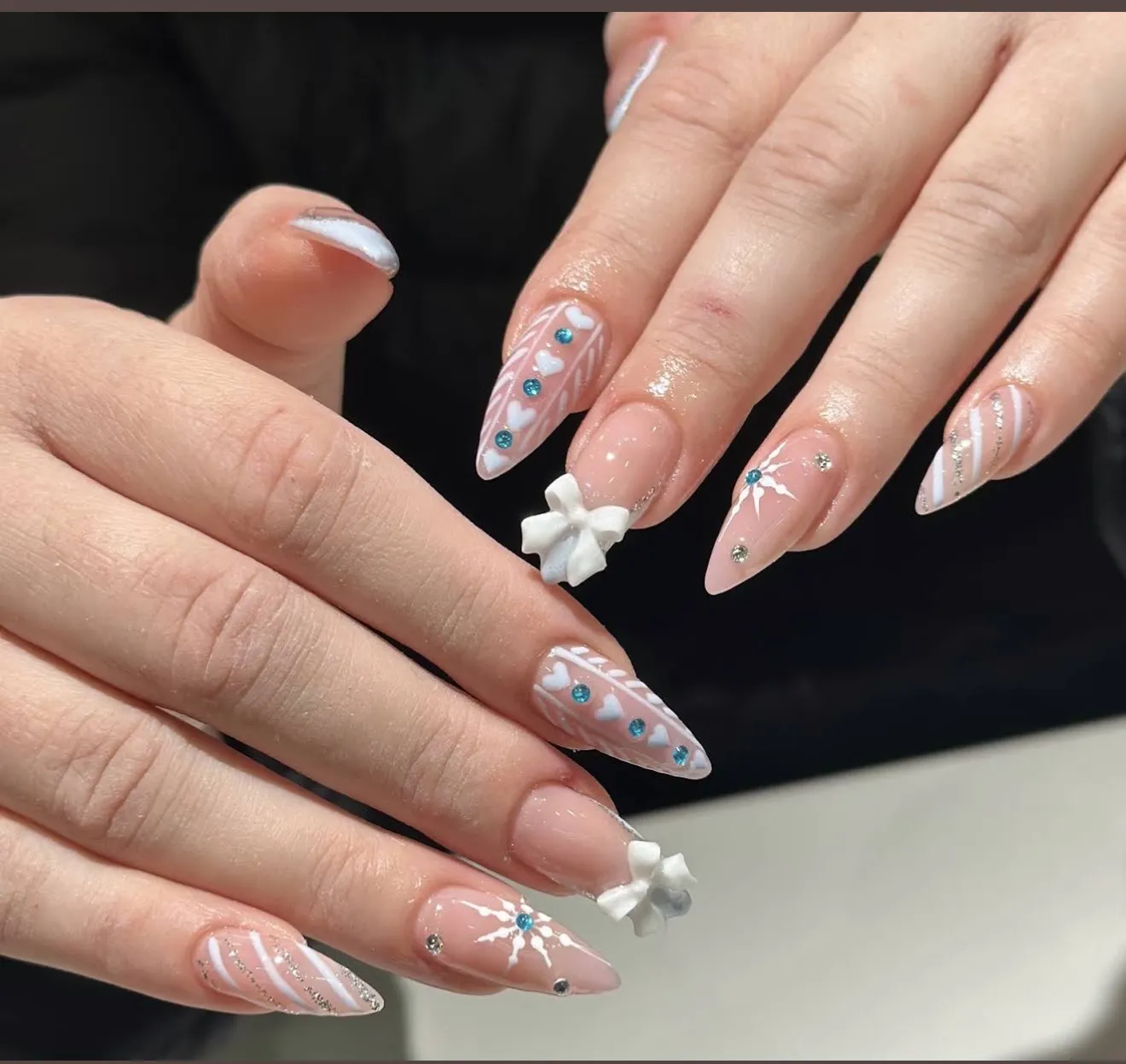 Sheer nude almond nails with white bows, hearts, snowflakes and blue crystals